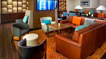 A hotel lobby with a seating area, a flat-screen TV, and a wall-mounted shelf with decorative items.
