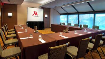 Un salón de conferencias con una pantalla grande mostrando el logotipo de Marriott, varias mesas con sillas y vistas amplias a través de grandes ventanales.