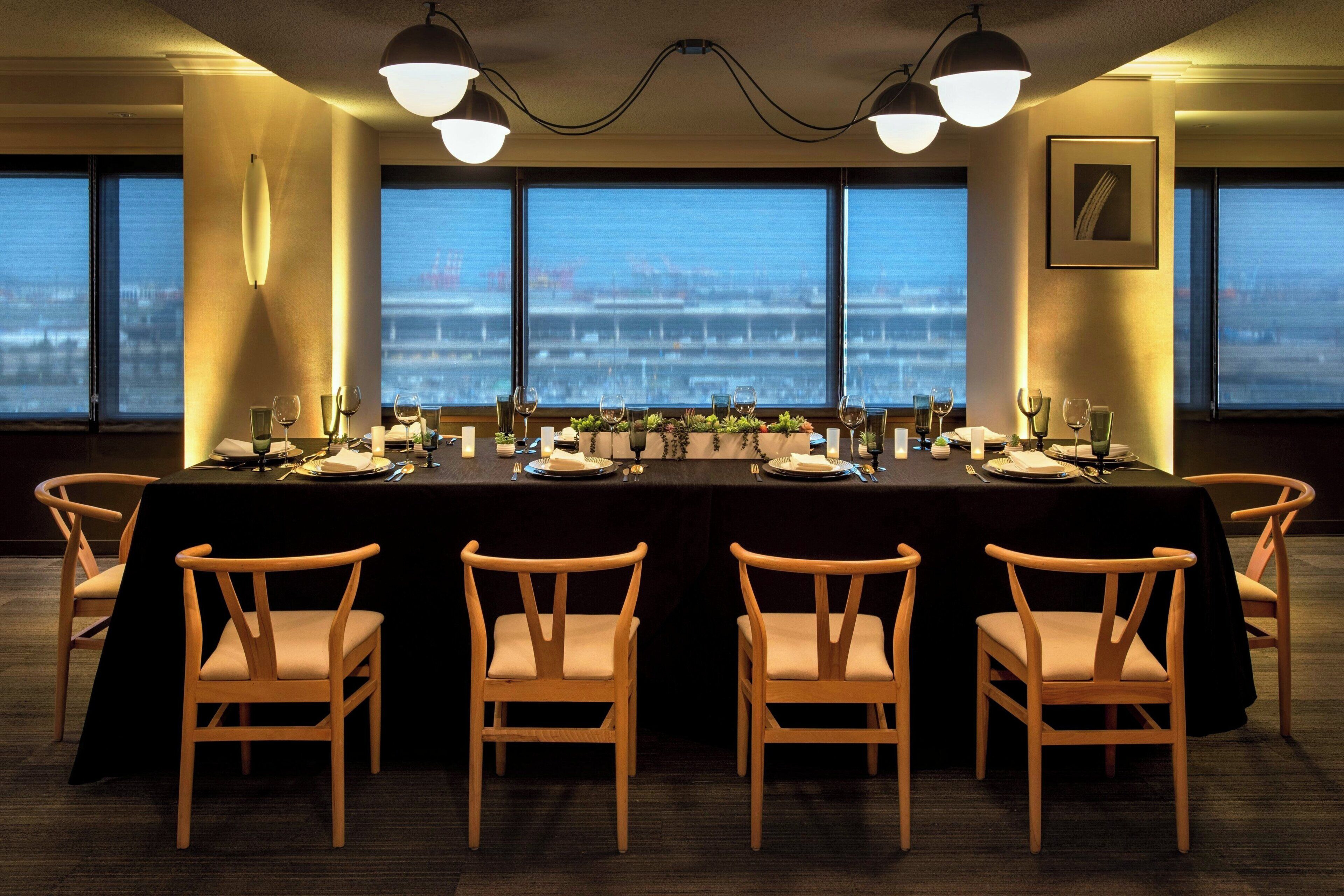 A conference room with a long table, six chairs, and large windows with a city view.
