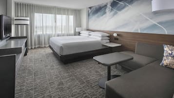 A modern hotel room with a large bed, a desk, a sofa, and a TV.