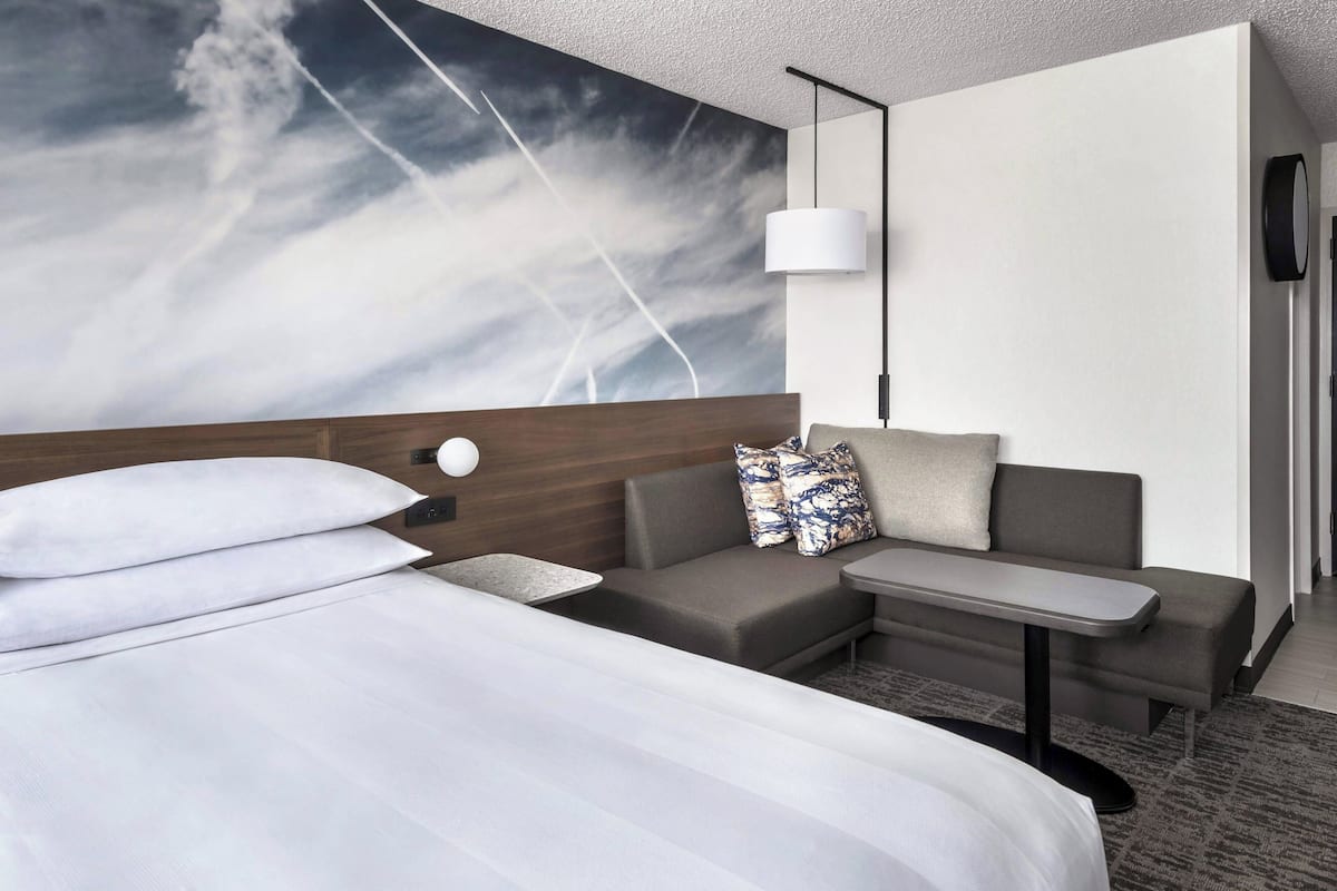 Una habitación de hotel moderna con una cama grande, un sofá, una mesita y una lámpara de pared.