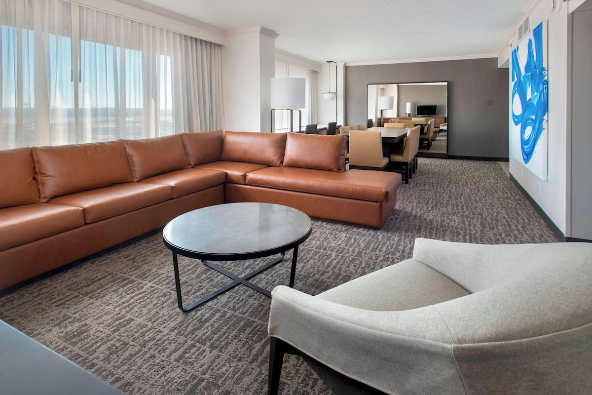 Una habitación de hotel moderna con un sofá modular, una mesa de centro redonda y un sillón individual.