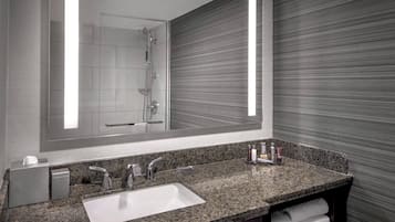 A modern bathroom with a granite countertop, a large mirror, a shower, and a towel rack.