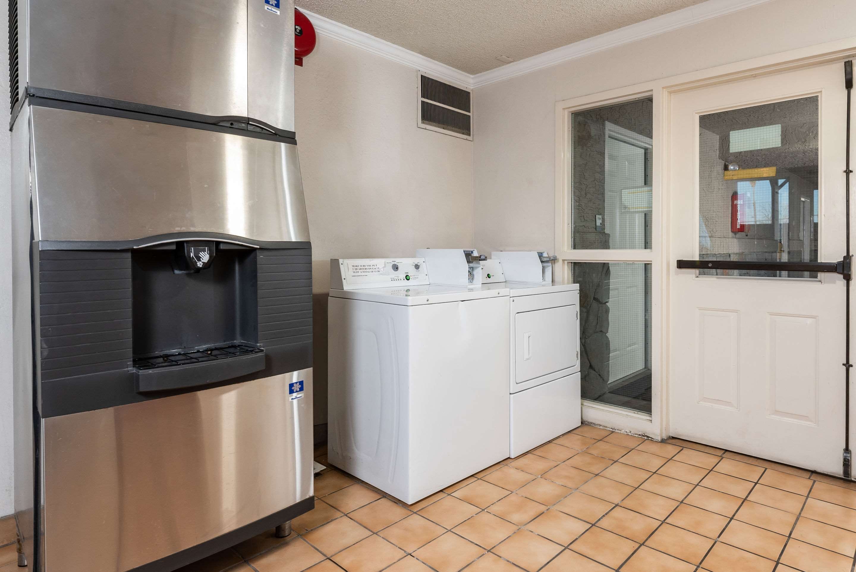 Une cuisine compacte équipée d’un réfrigérateur en acier inoxydable, d’un lave-linge et d’une porte donnant sur un balcon.