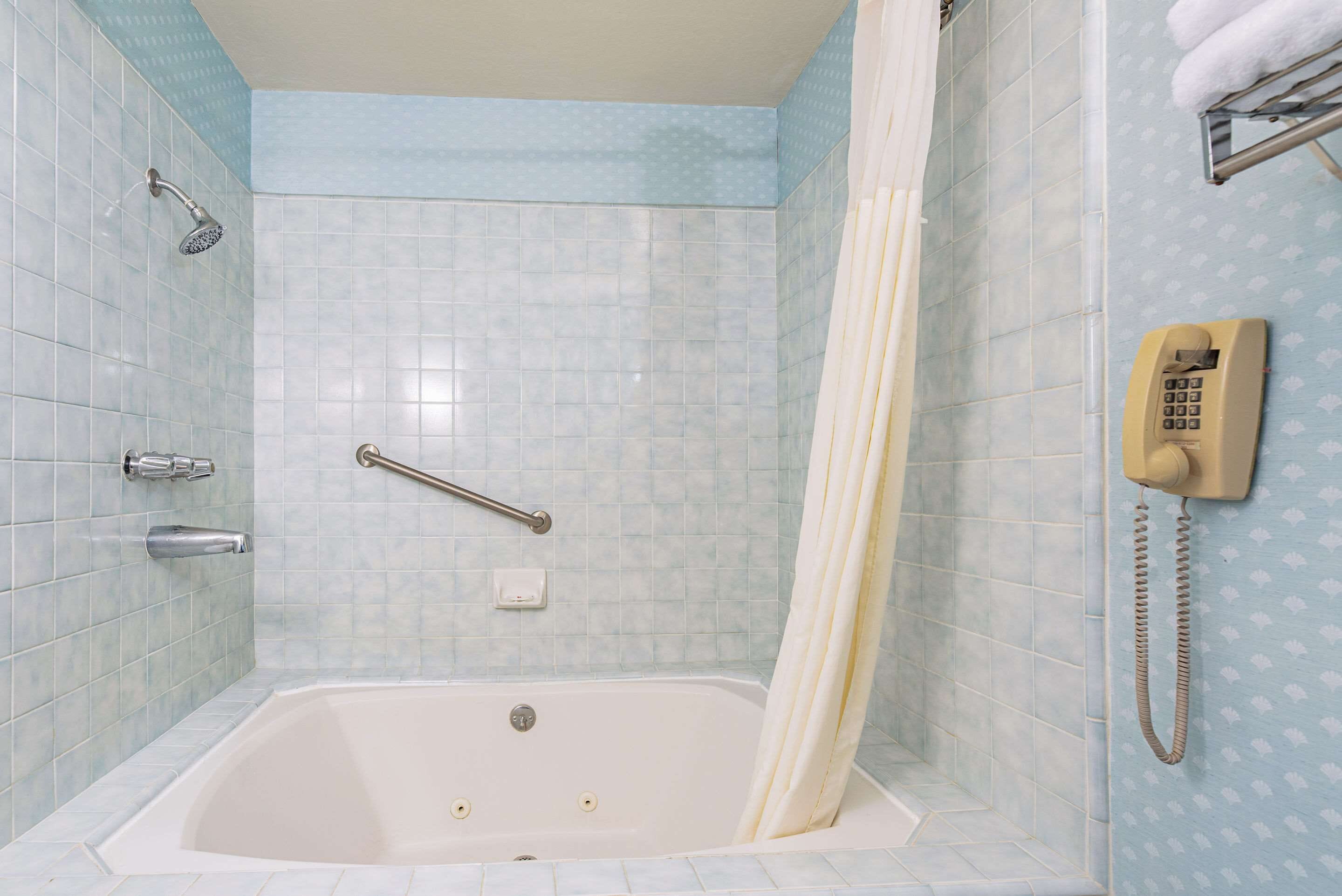 Ein Badezimmer mit Badewanne, Duschkopf, Handläufer und Telefon.