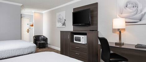 Habitación de hotel con dos camas, televisión, microondas, escritorio con silla y obras de arte en las paredes.