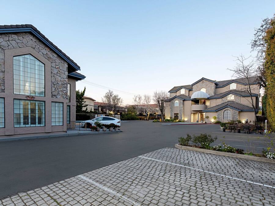 A residential street with stone facades, a parked car, and a paved driveway.
