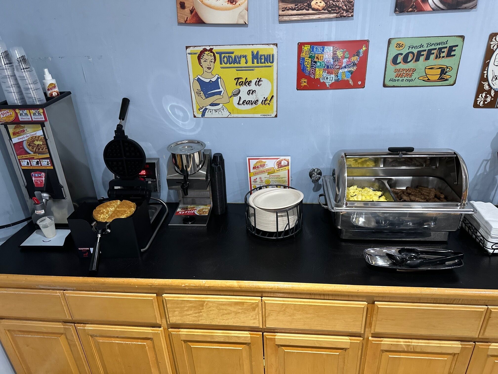 A breakfast bar with a waffle maker, syrup dispenser, and a coffee station.