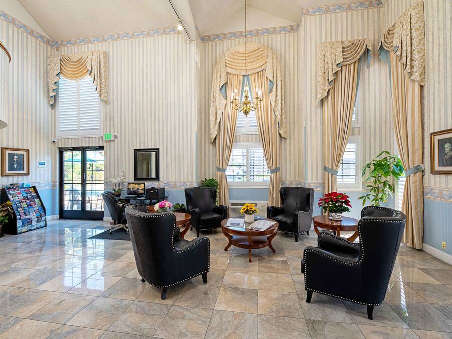 A spacious lobby with striped wallpaper, large windows with curtains, and a central seating area with black upholstered chairs and a round wooden table.