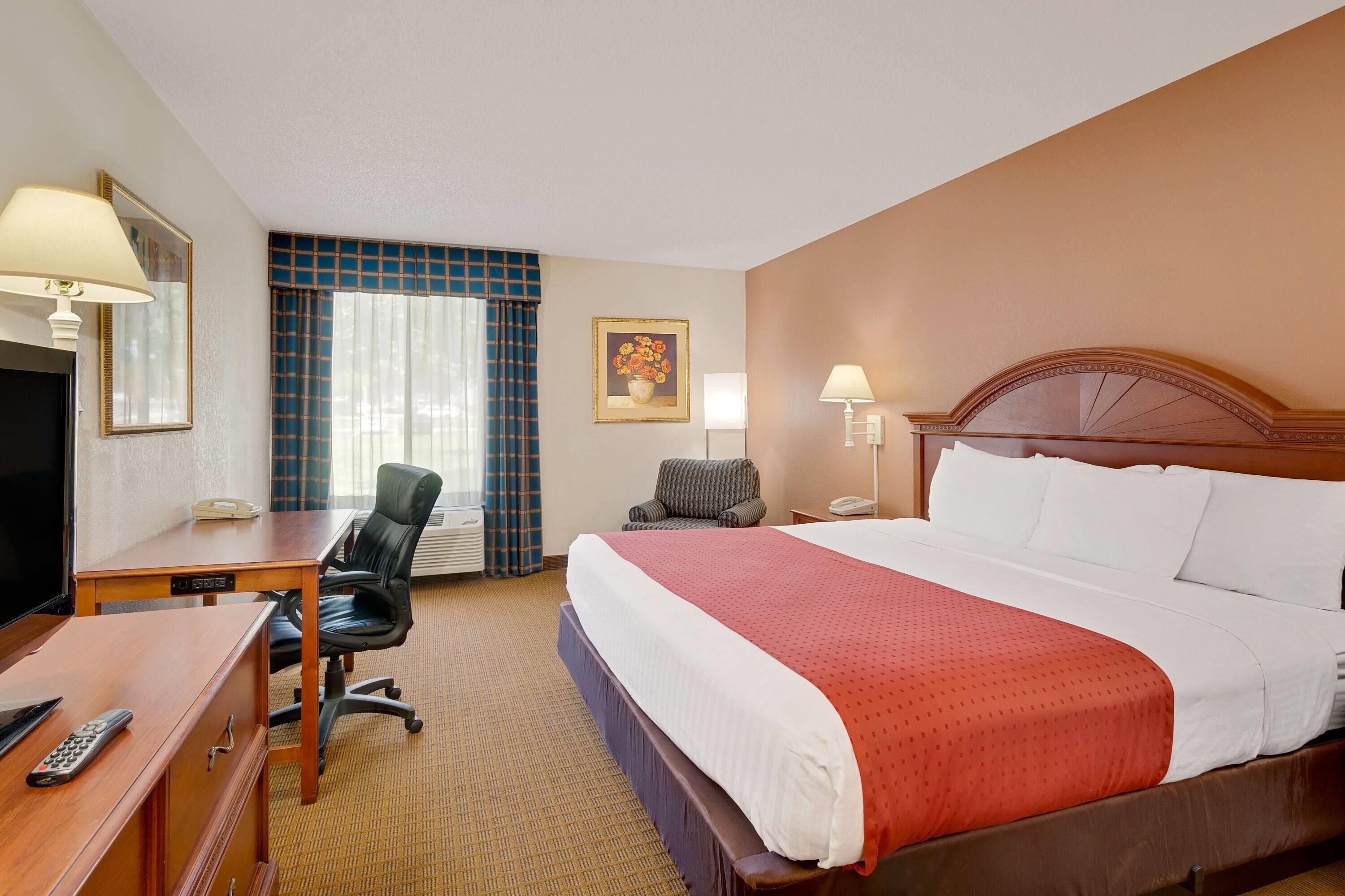A hotel room with a bed, desk, chair, TV, and a painting on the wall.