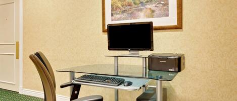 A hotel room with a glass desk, a computer, a chair, and a framed picture on the wall.