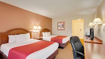 A hotel room with two beds, a desk, a chair, a TV, and a lamp.