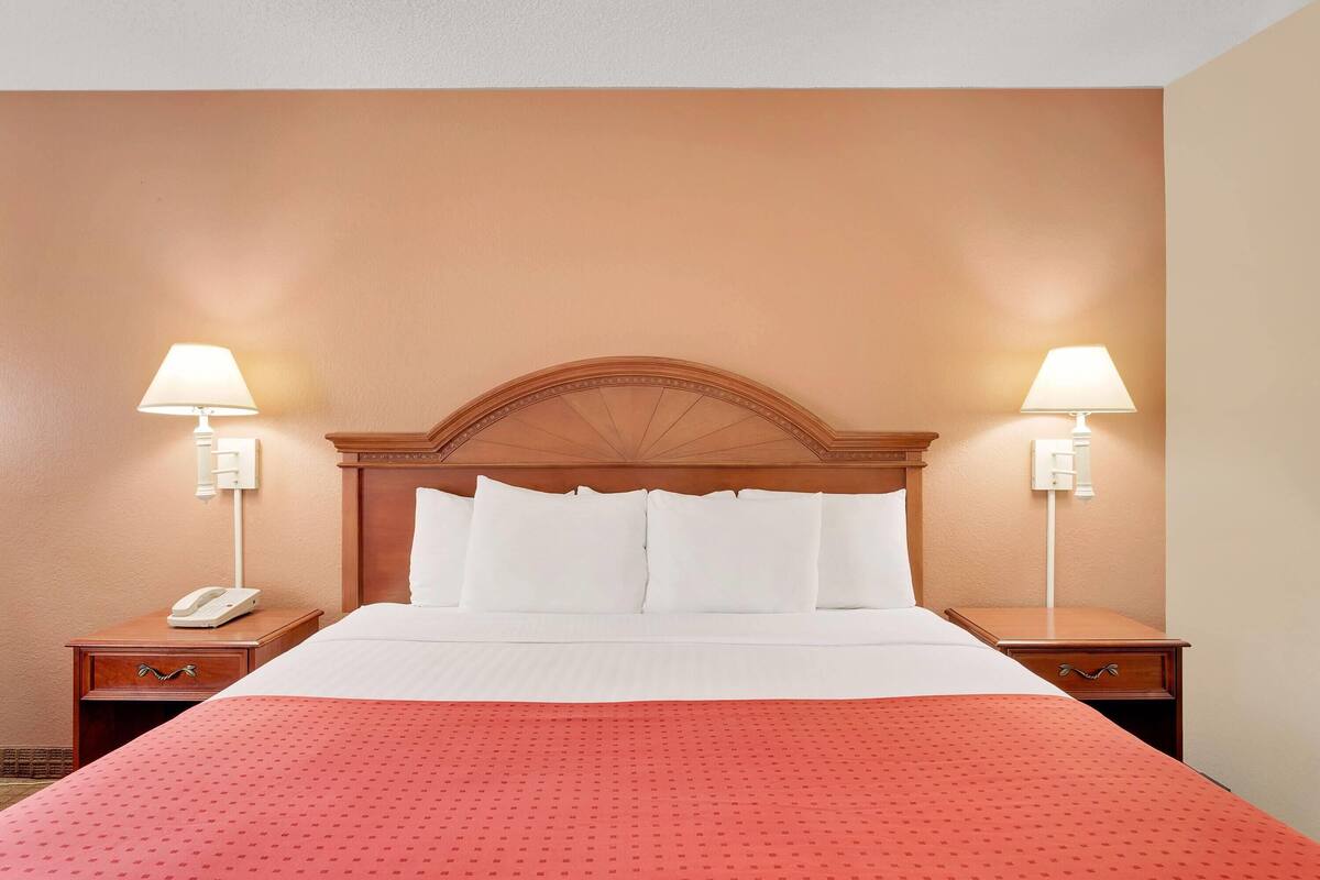 Una habitación de hotel con una cama grande, dos mesitas de noche, un teléfono y lámparas fijadas a la pared.
