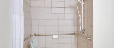 A shower area with a grab bar, a white chair, and a handheld showerhead.