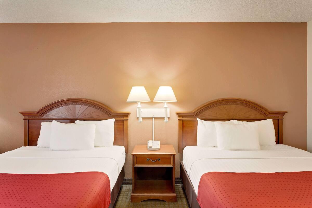 Habitación de hotel con dos camas, una mesita de noche con lámparas y cabecero de madera.