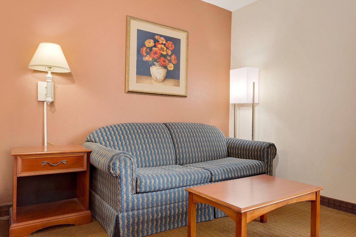 Una habitación con un sofá estampado, una mesita de noche de madera, una mesa, una lámpara y un cuadro floral enmarcado en la pared.
