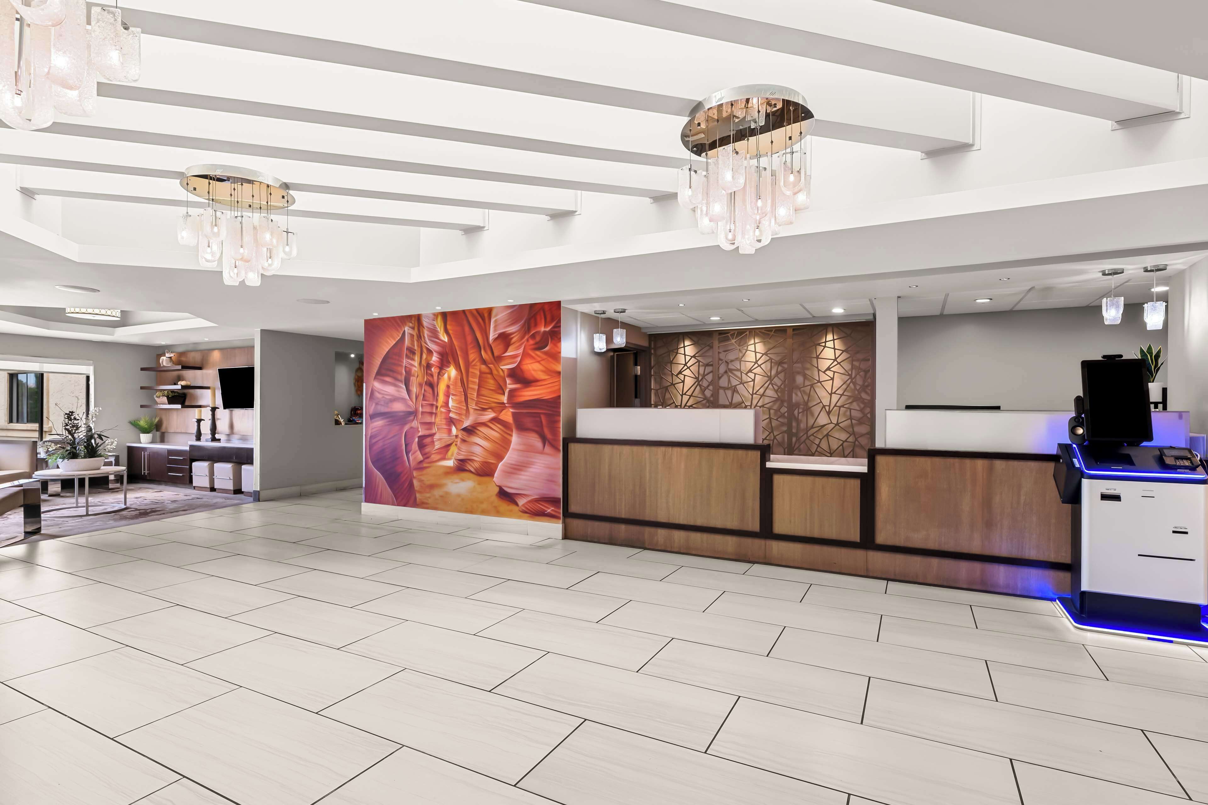 A modern hotel lobby with a reception desk, a large abstract mural, and a chandelier.