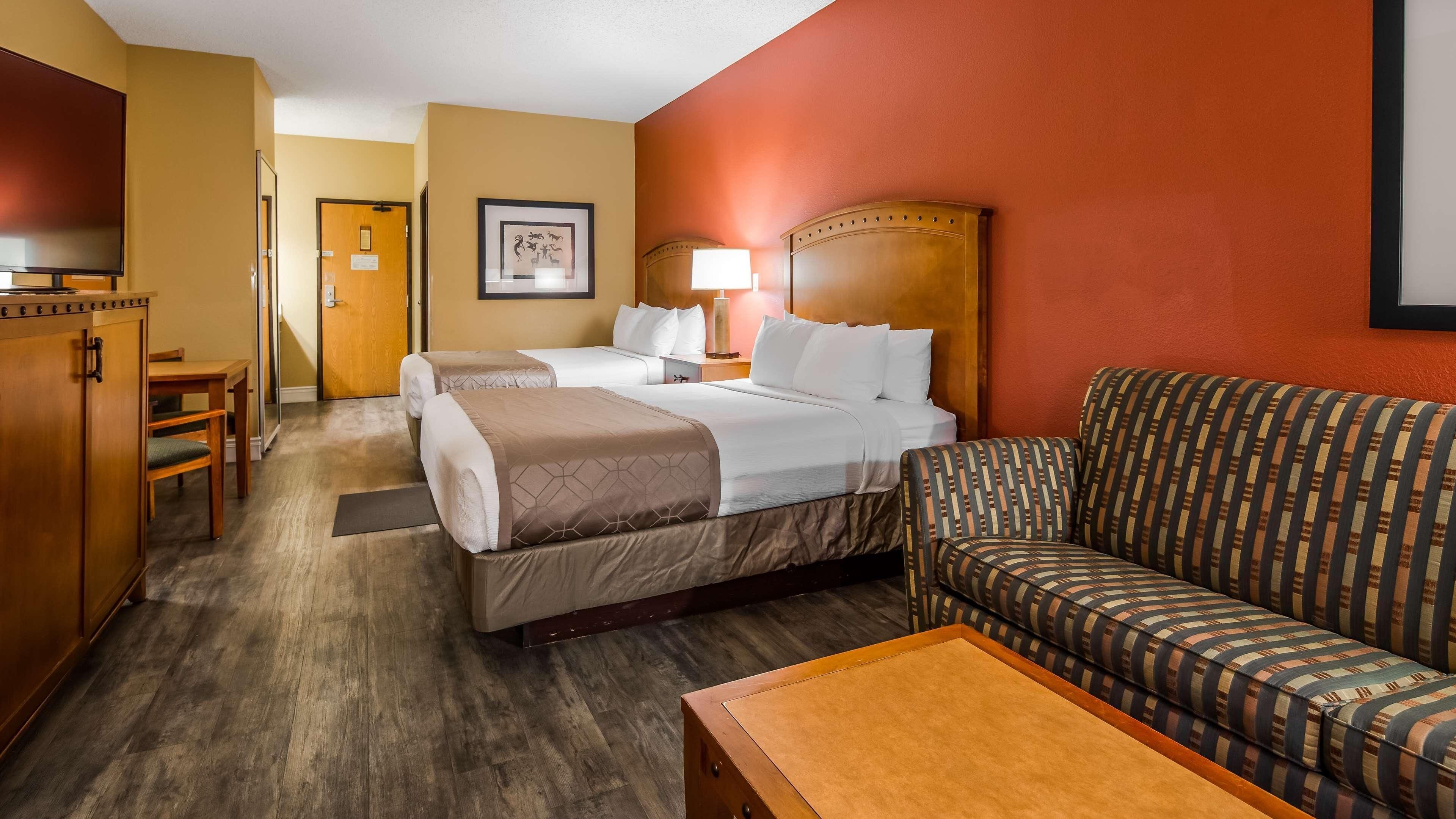 A hotel room with two beds, a sofa, a wooden table, and a TV.