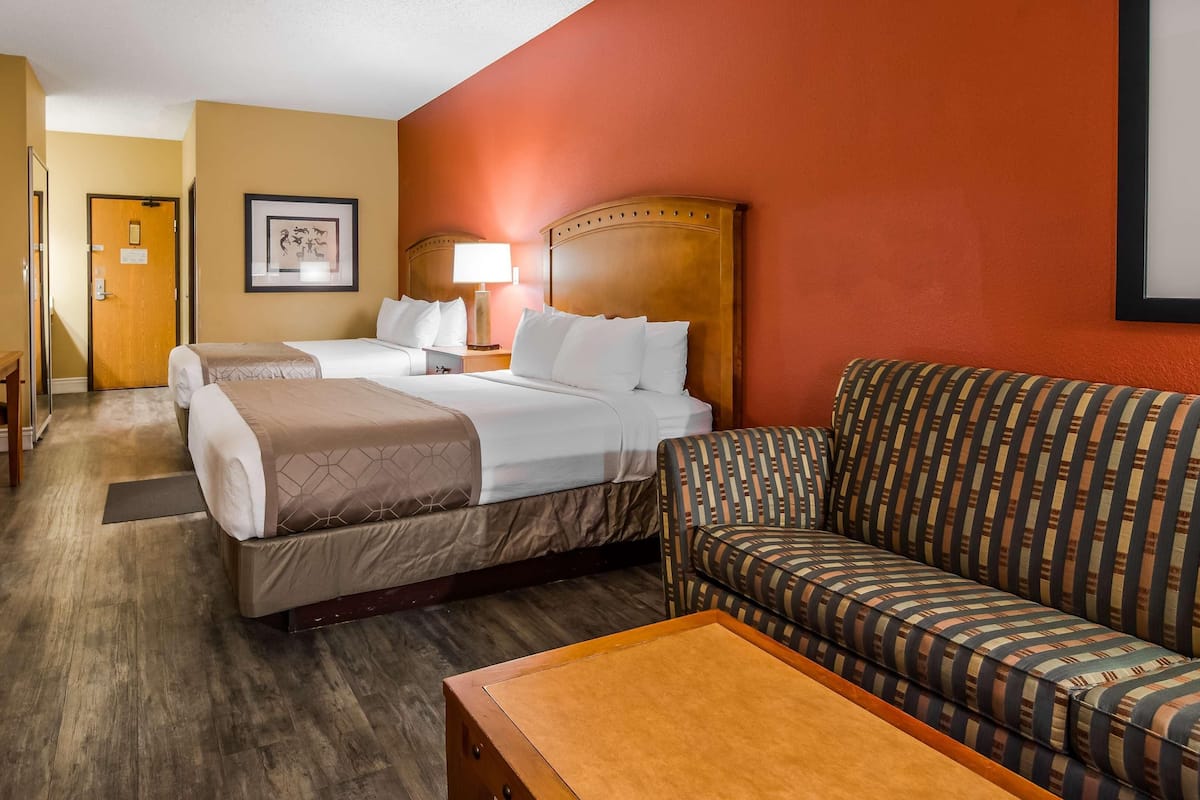 A hotel room with two beds, a sofa, a wooden table, and a TV.