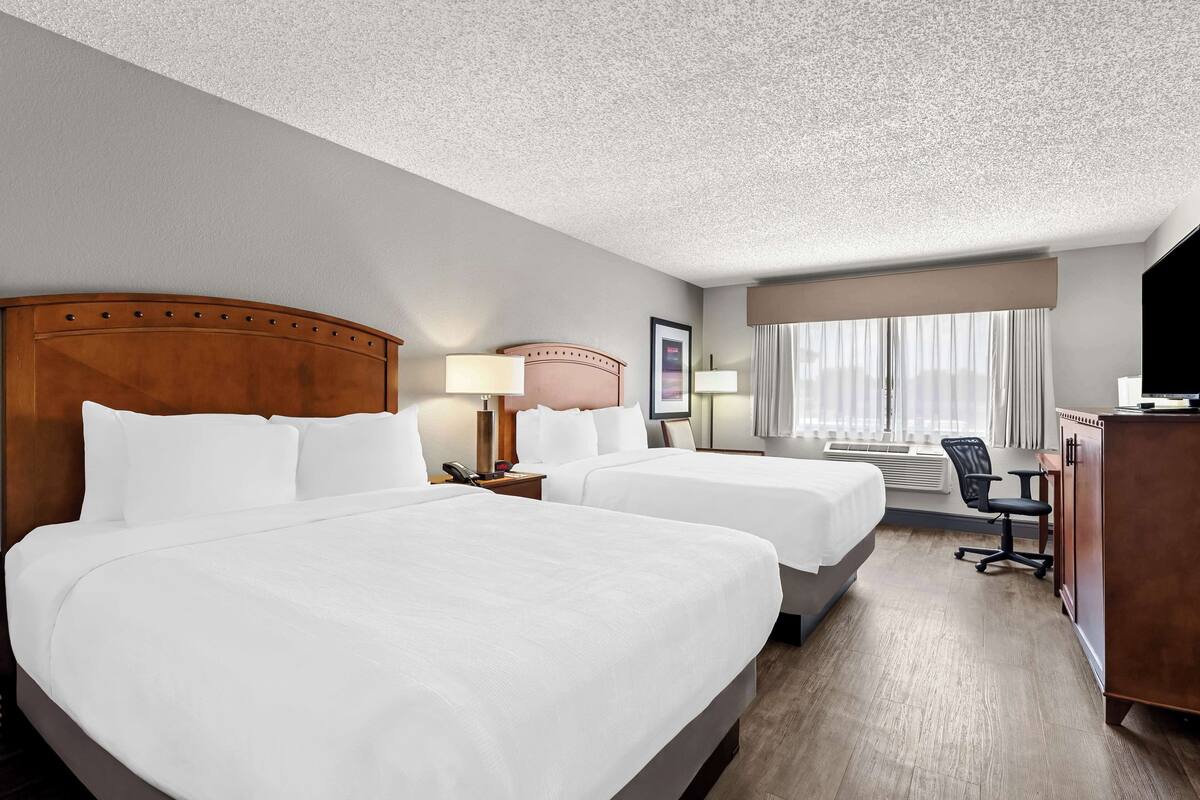 A hotel room with two beds, a desk, a chair, a television, and a window with curtains.