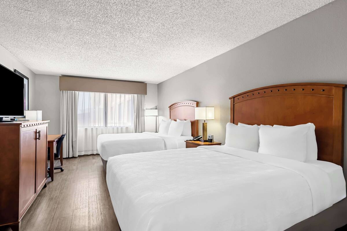 A hotel room with two beds, a desk, a TV, and a lamp.