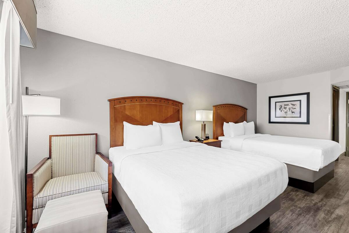 A hotel room with a large bed, two smaller beds, a chair, a desk, and a lamp.