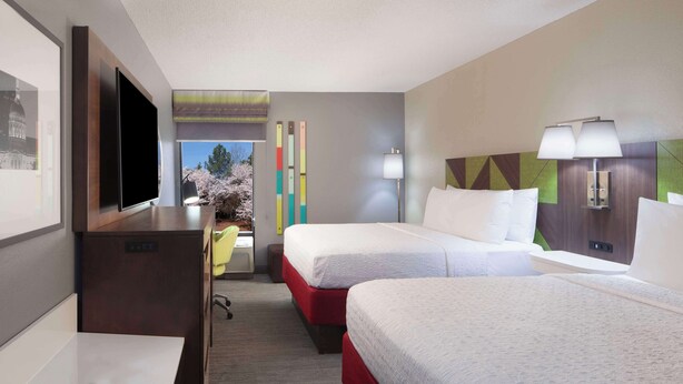 Habitación de hotel con dos camas, un escritorio, un televisor y ventana con vista a árboles.