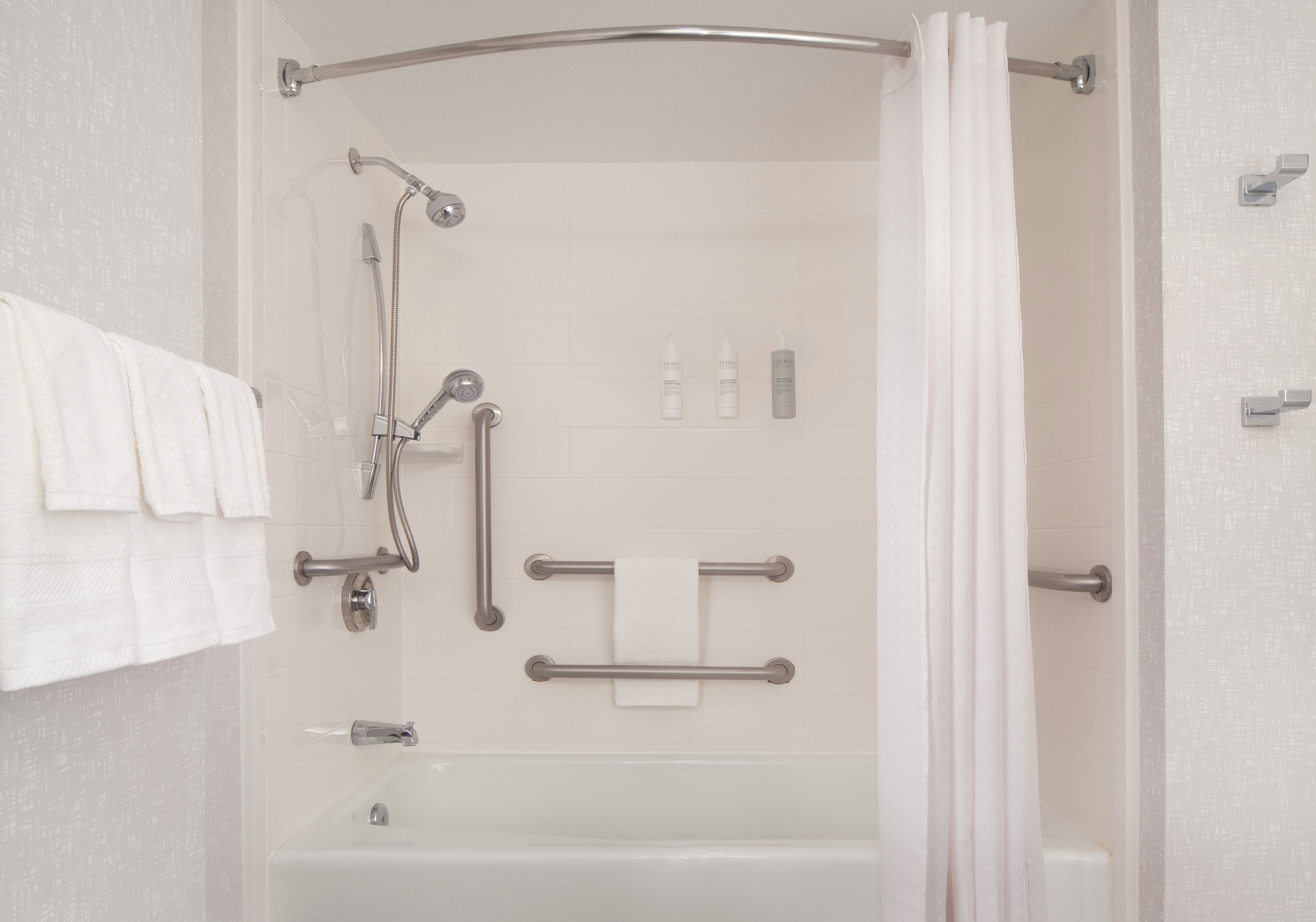 A walk-in shower with a grab bar, a handheld showerhead, a handheld faucet, and a towel rack.