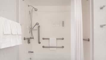 A walk-in shower with a grab bar, a handheld showerhead, a handheld faucet, and a towel rack.