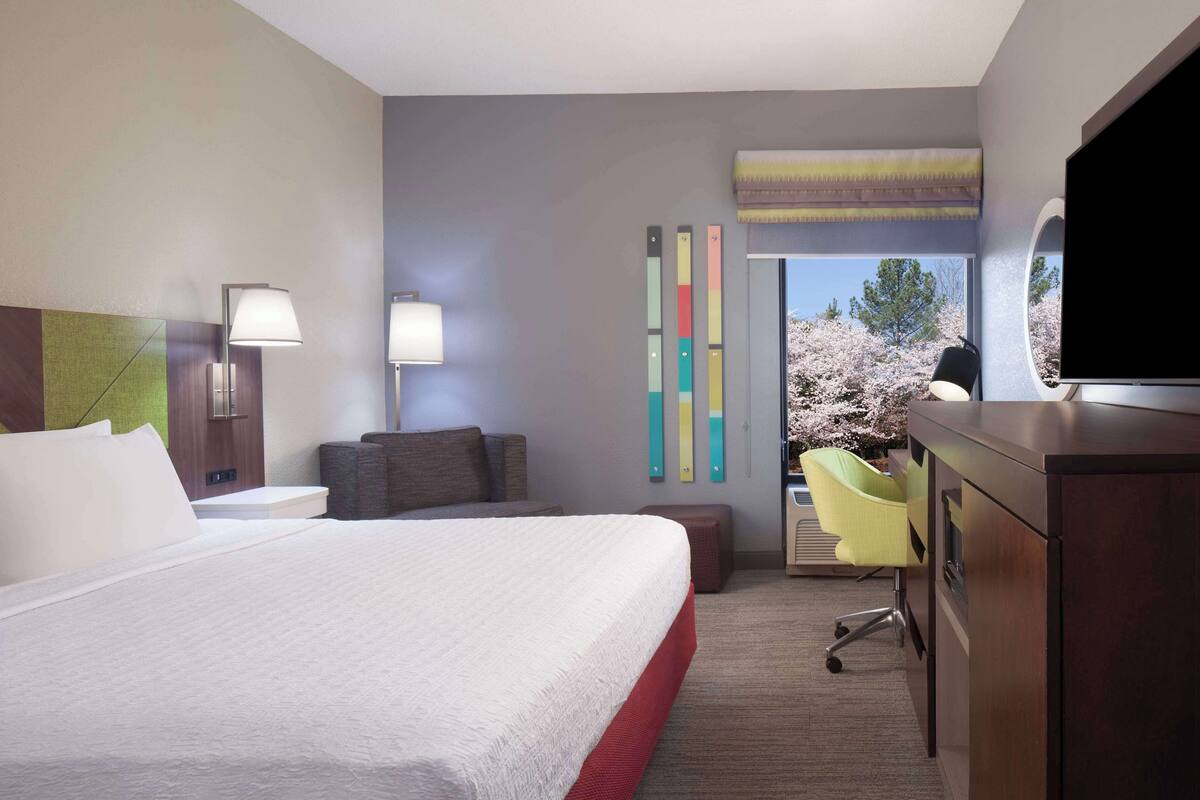 A hotel room with a large bed, bedside lamps, a TV, a desk, and a view of cherry blossoms.