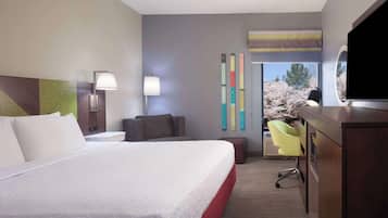 A hotel room with a large bed, bedside lamps, a TV, a desk, and a view of cherry blossoms.