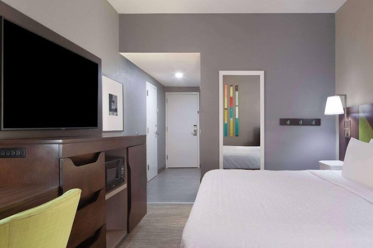 A hotel room with a bed, a TV, a desk, and a door leading to another room.