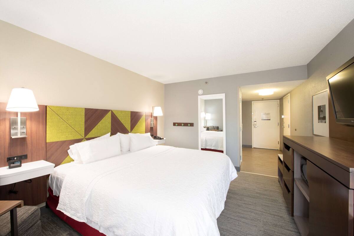 A hotel room with a bed, bedside table, lamp, and a mirror.