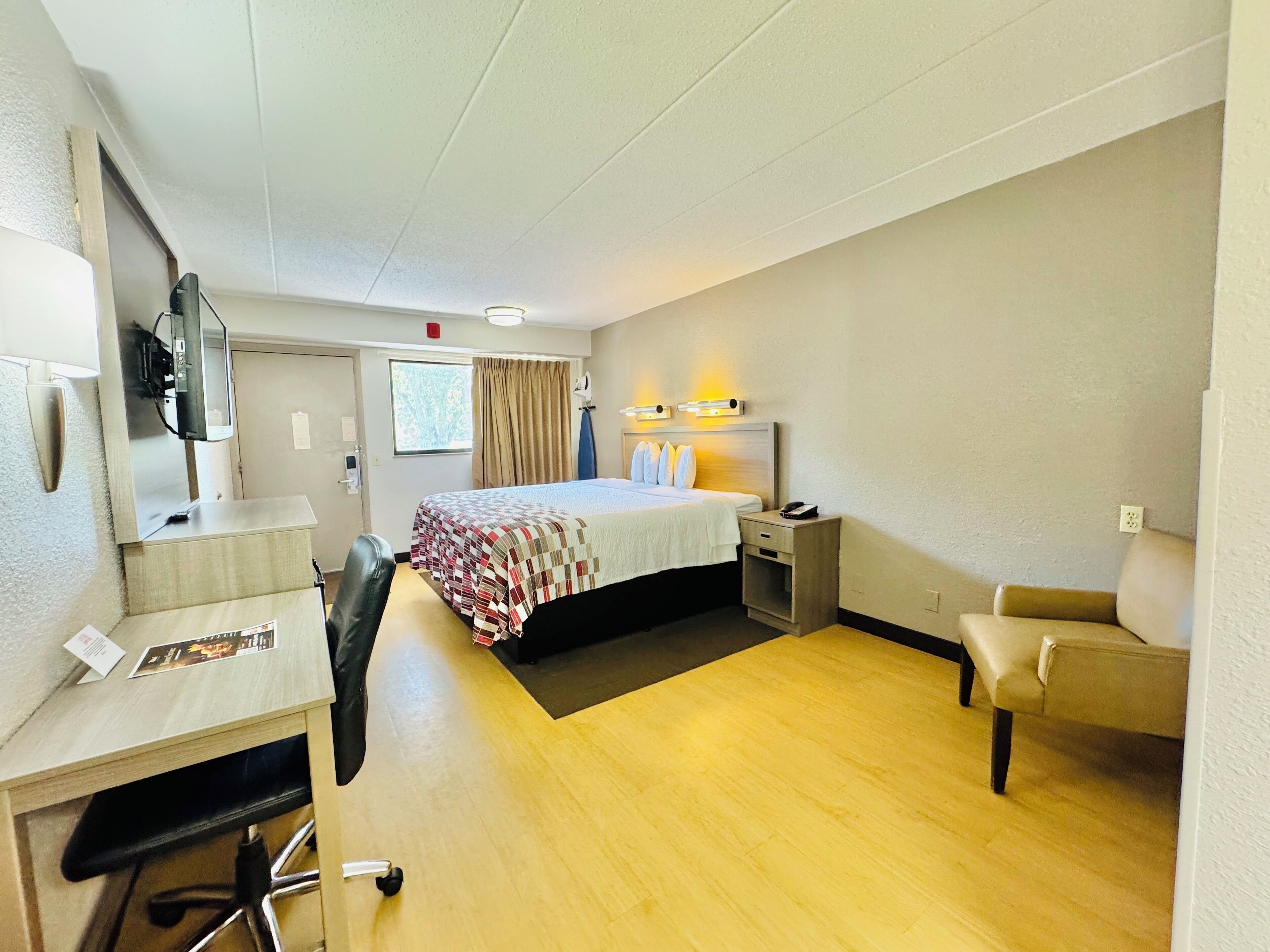 A hotel room with a bed, desk, chair, and a small table.