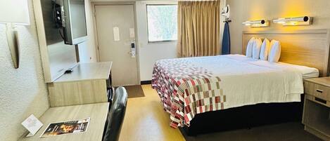 A hotel room with a bed, desk, chair, television, and a window with curtains.