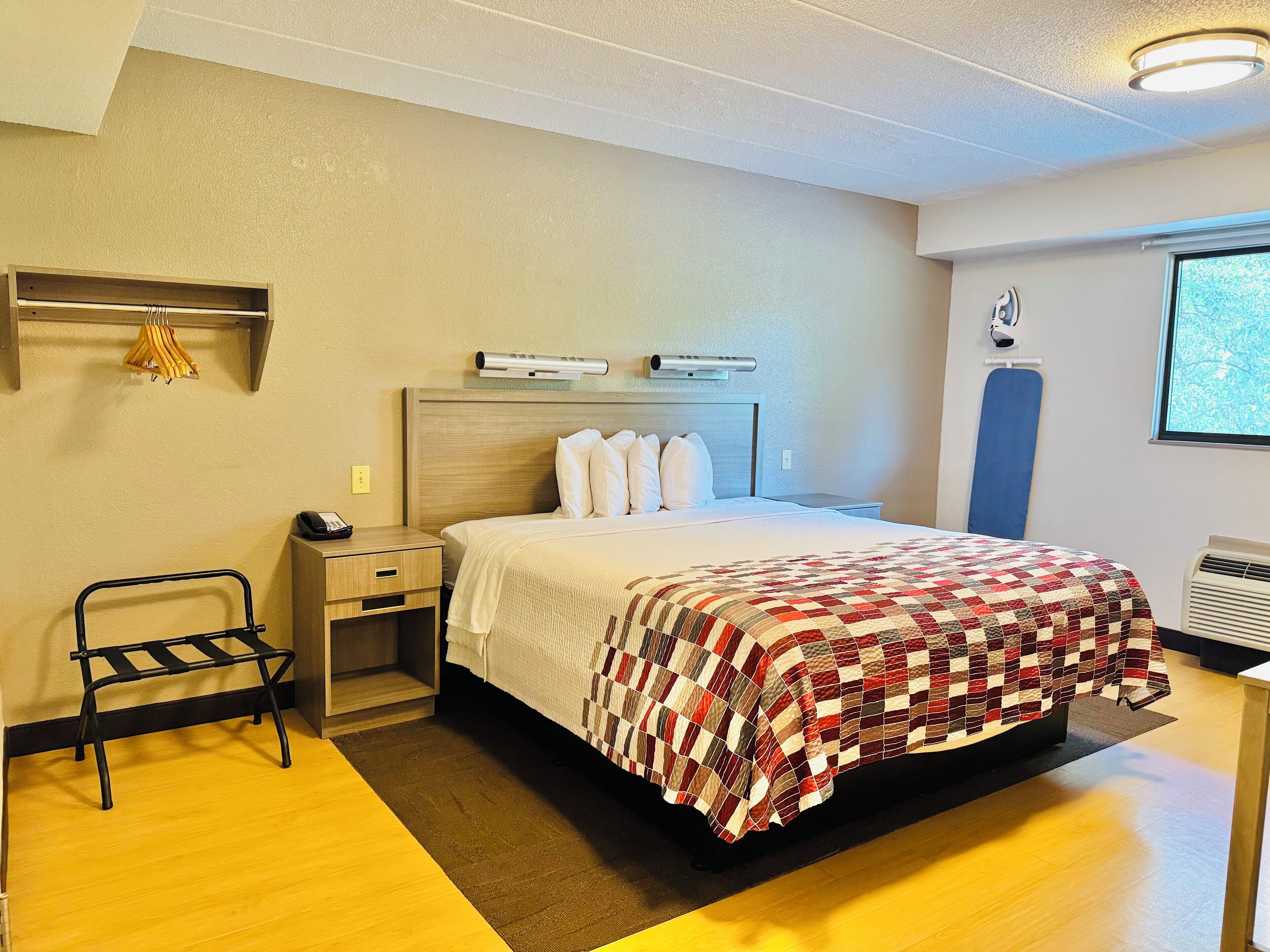 Hotellihuone, jossa on sänky, yöpöytä, tuoli, työpöytä ja ikkuna.