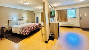 Une chambre d’hôtel comprenant un lit, une table de chevet, une télévision, un appareil de climatisation et une fenêtre avec des rideaux.