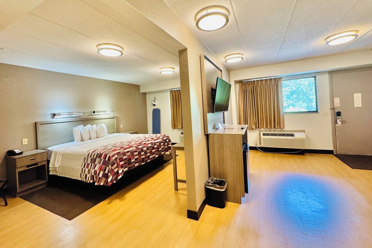 Habitación de hotel con cama, mesita de noche, televisor, aire acondicionado y ventana con cortinas.
