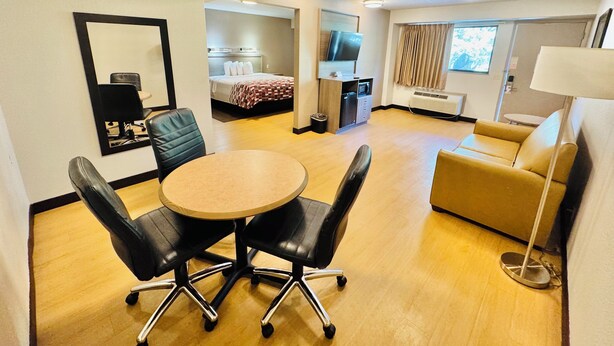 Une chambre d’hôtel avec une table ronde, deux chaises noires, un canapé, une télévision, un minibar et un miroir.