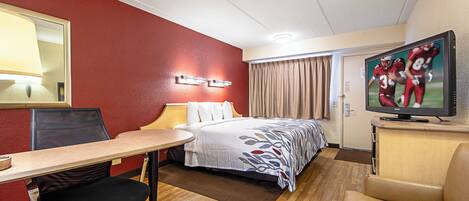 A hotel room with a bed, desk, chair, television, and a mirror.