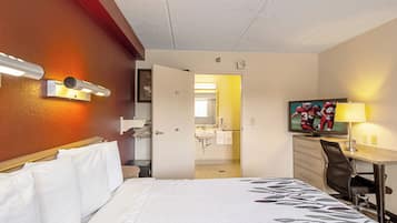A hotel room with a bed, a desk, a chair, a television, and a bathroom visible through an open door.