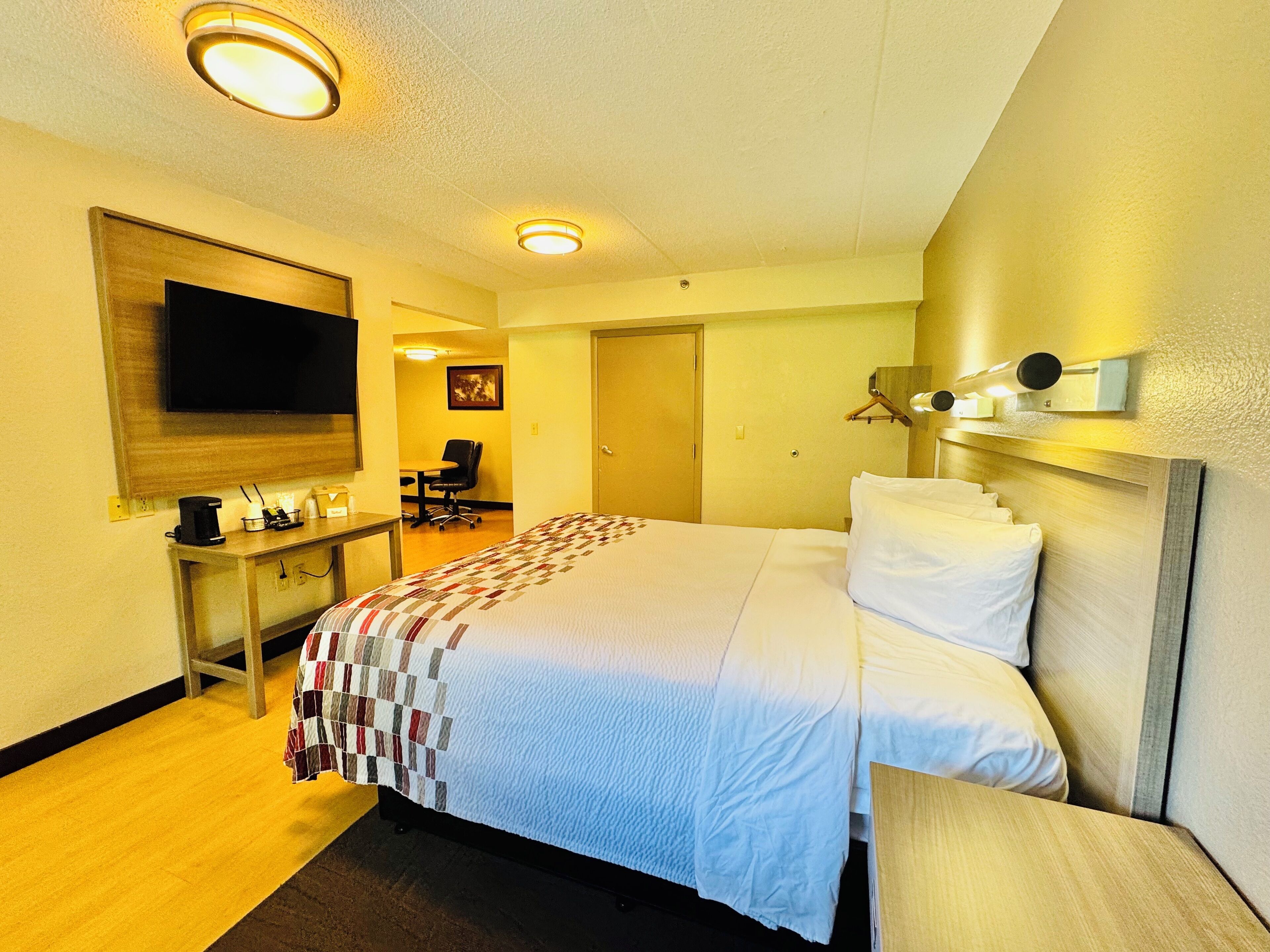 Una habitación de hotel con cama, mesita de noche, escritorio, silla y televisor en la pared.
