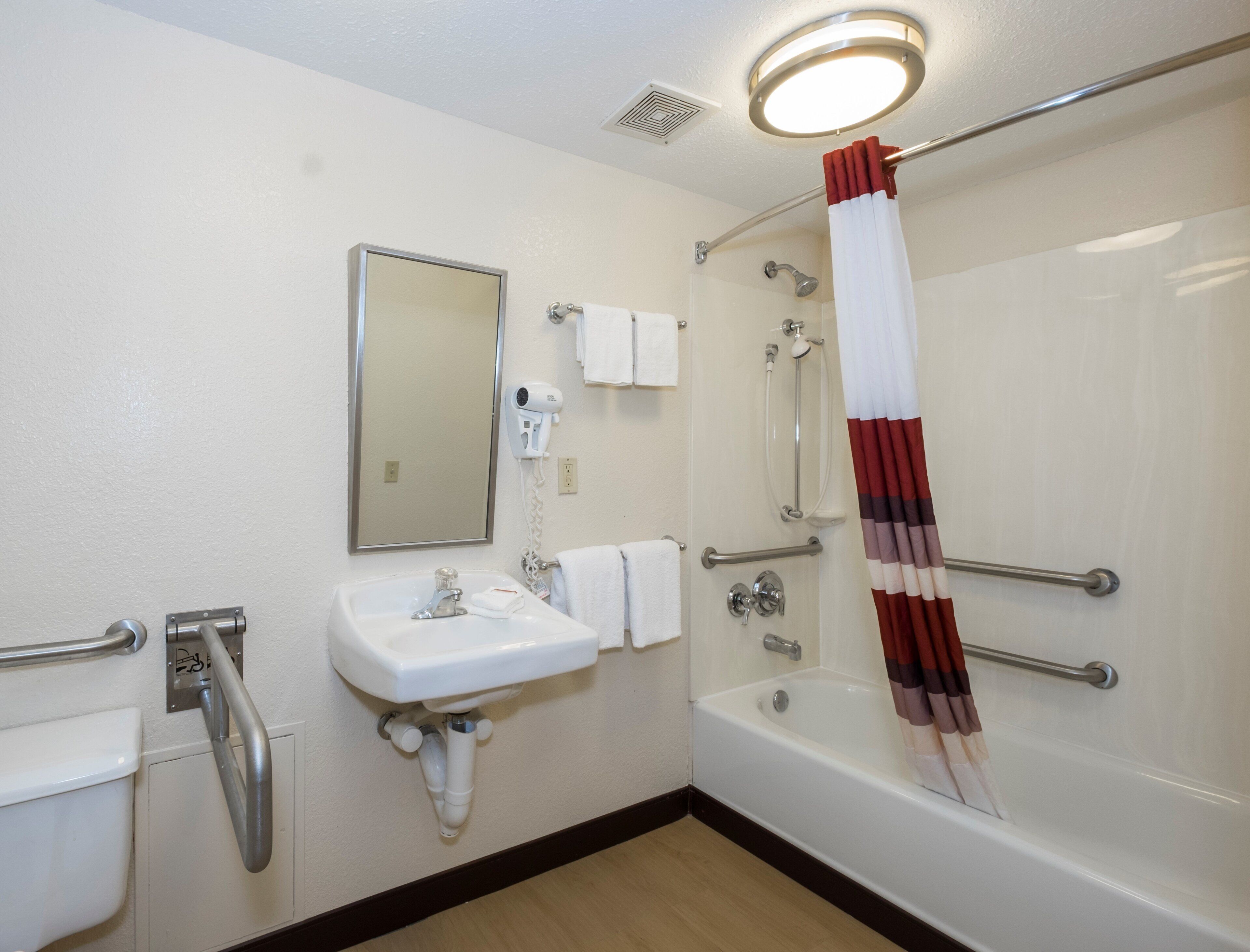 A bathroom with a sink, mirror, towel rack, shower, and a hand dryer.