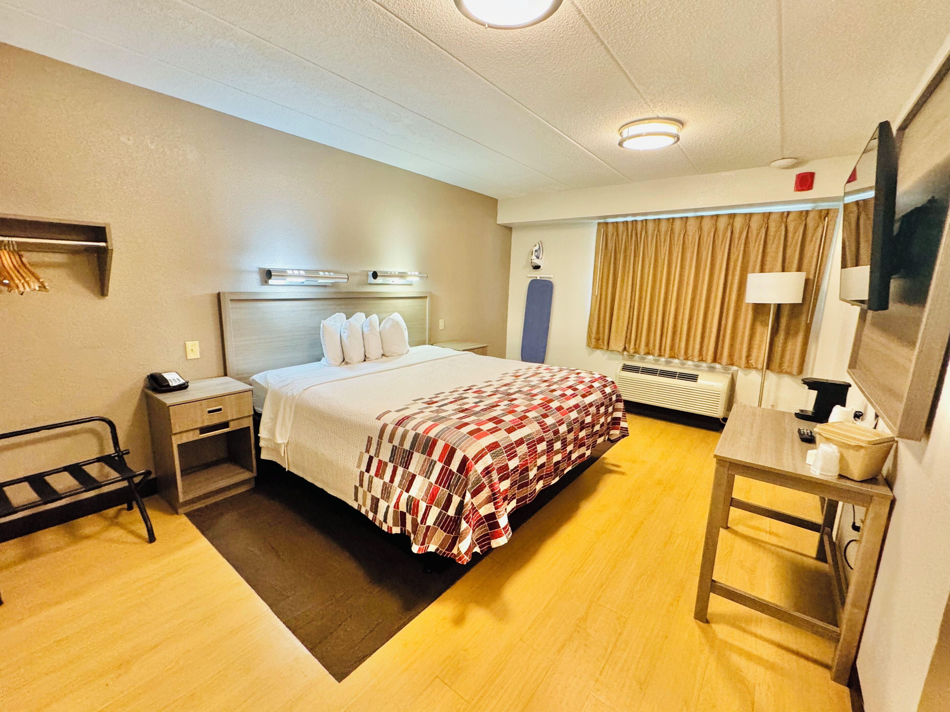 A hotel room with a bed, bedside table, lamp, and a desk with a chair.