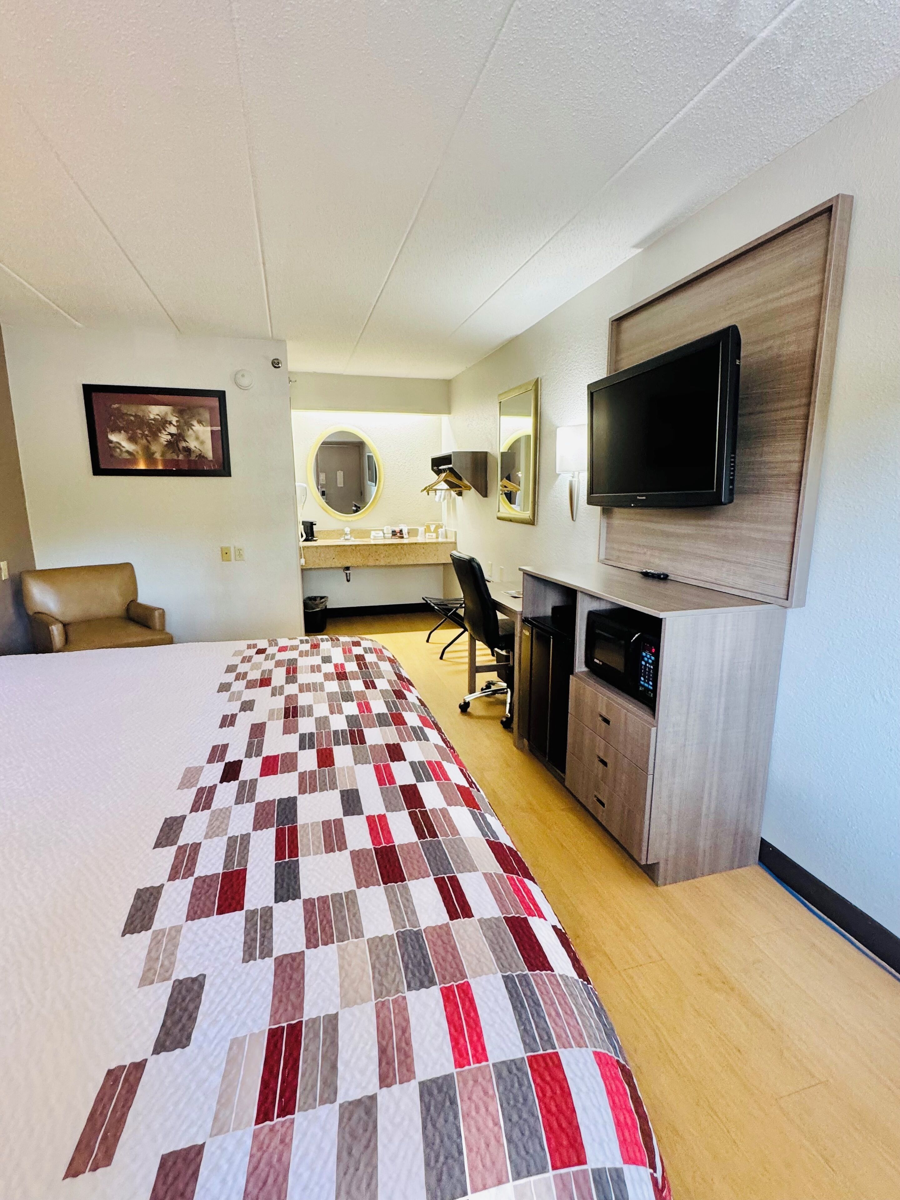 A hotel room with a large bed, a desk with a computer, a TV, and a chair.
