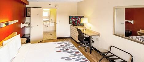 A hotel room with a bed, desk, chair, and a television.