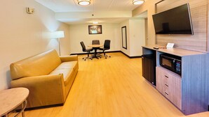 Une chambre d’hôtel comprenant un canapé, une petite table, une télévision, un four à micro-ondes et un coin repas avec des chaises et une table.