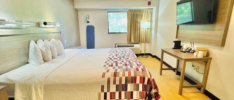 Una habitación de hotel con cama, escritorio, televisor y ventana con cortinas.