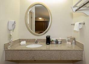 Une salle de bain dotée d’un comptoir en granit, d’un miroir rond, d’un sèche-cheveux, d’une machine à café et d’articles de toilette.
