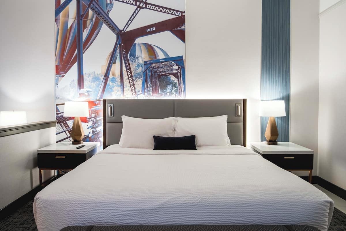 A hotel room with a large bed, two bedside tables with lamps, and a mural of a bridge on the wall.